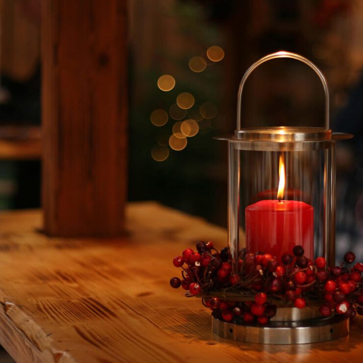 Red candle, lit, on wooden plank table.