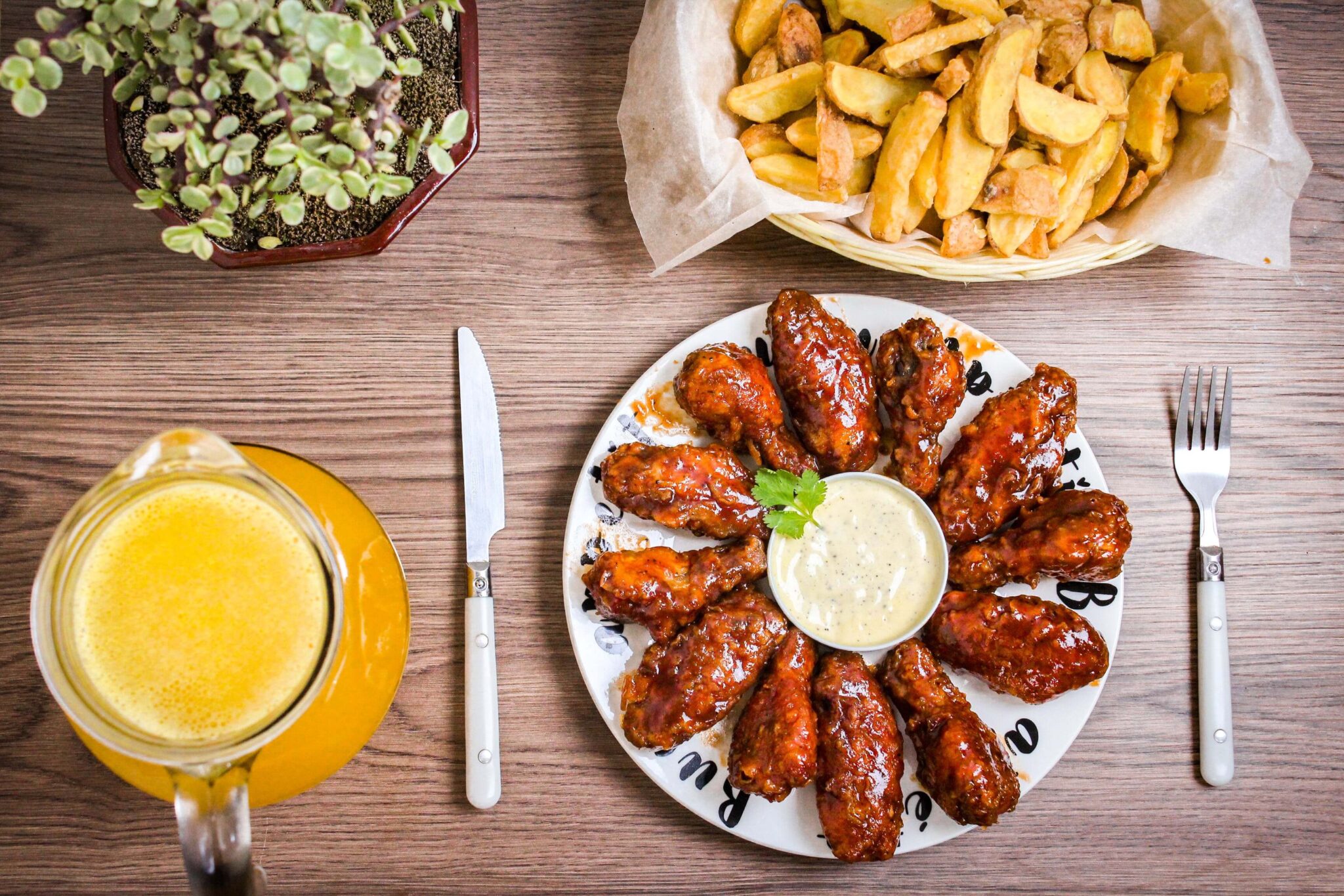 Plate of wings on wooden tabletop along with side dishes.