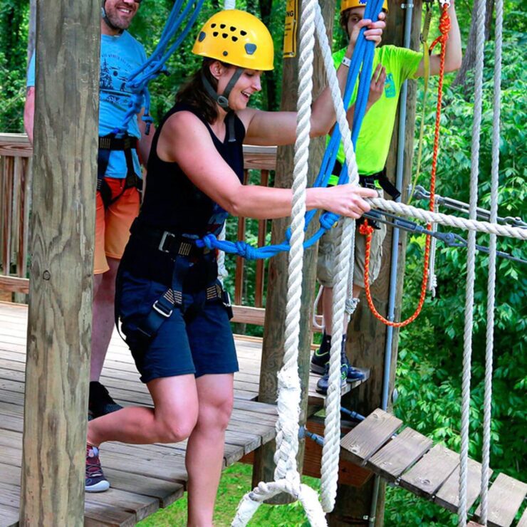 Woman in yellow helmet and harness steps off platform on ropes course
